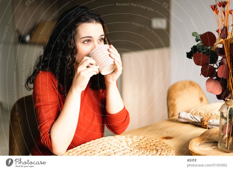 Young woman drinking a coffee sitting at the table cup tea breakfast beverage female kitchen looking away dreamy home lifestyle holding hot girl portrait