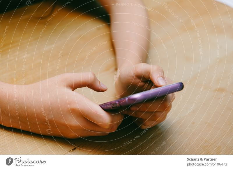 Hands of a young person hold purple colored smartphone. The arms are placed on a wooden table top. Chat Puberty 13 - 18 years Youth (Young adults)