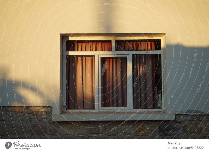 Facade in beige and natural colors in the light of the evening sun with white window with red curtain in Cunda near Ayvalik on the Aegean Sea in the province of Balikesir in Turkey