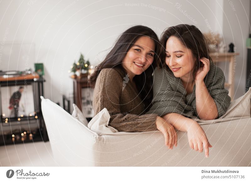 Two women sitting on a couch at cozy home apartment. Family spending time at home. Portrait of sisters smiling in modern minimal interior. comfortable