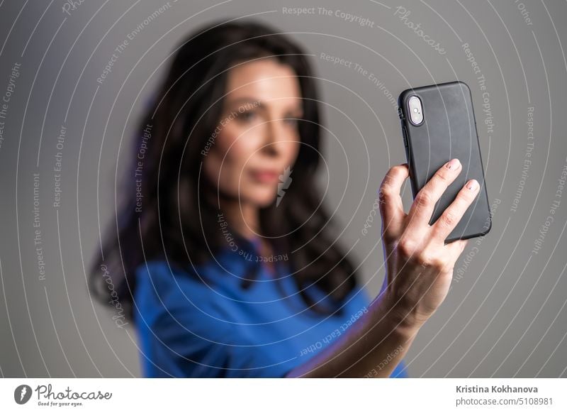 Smiling happy adult woman making selfie on smartphone over grey background. Technology, mobile device, social networks concept person mobile phone communication