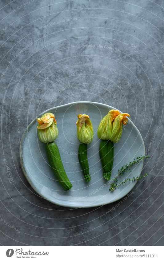 Three zucchini flowers on plate on stone background. vegetable three vertical photo top view stone effect gray plate courgette green healthy harvest yellow