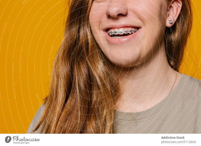 Smiling girl with brackets with long hair in studio cheerful happy smile joy positive glad optimist toothy smile young friendly vivid colorful yellow background