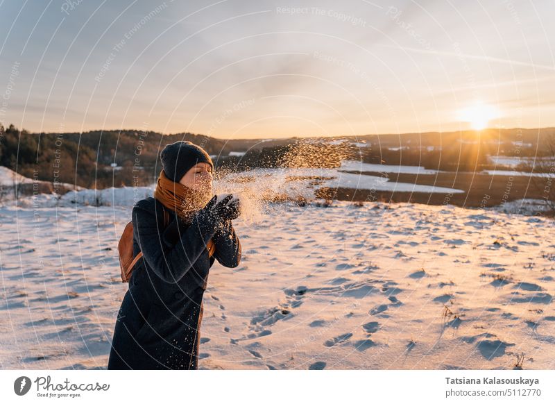 A woman blows snow from her palms on a snow-covered field in winter female people person European White adult hold mid adult one Single person orange cold Enjoy