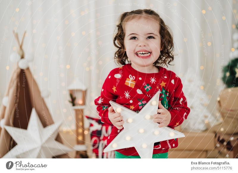 smiling little girl at home holding star during christmas time child presents happy gift cheerful cute 2 kid children family december decoration indoors smile