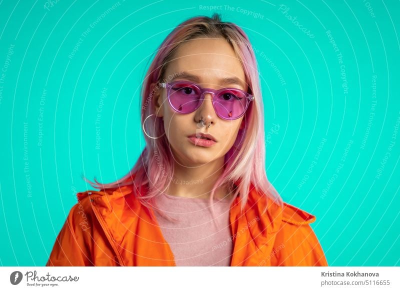 Portrait of pretty unusual woman with dyed hair on blue studio background. Trendy neon colorful teenager with piercing, eyewear. Vibrant shot. attractive