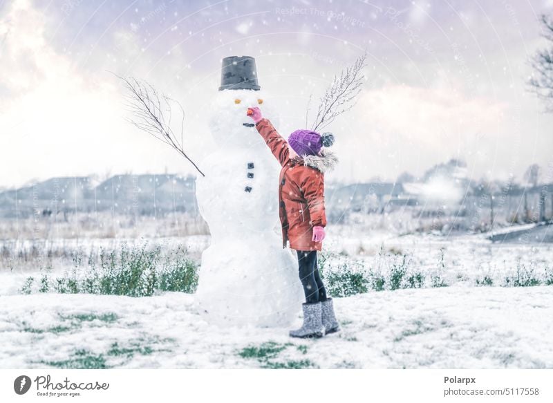 Little girl adding a carrot for the snowman nose sunset frost young purple caucasian lifestyle female frosty leisure children hat snowfall wintertime weather
