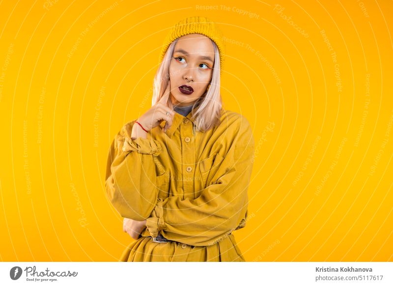 Thinking woman looking up and around on yellow background. Worried contemplative face expressions. Pretty girl model with unusual trendy appearance. thinking
