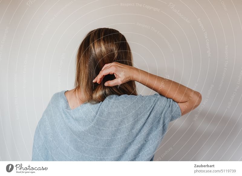 Woman shot from behind, hand in hair, wearing light blue sweater against neutral background Behind rear view arm lifted Hand Painting (action, work) frisky