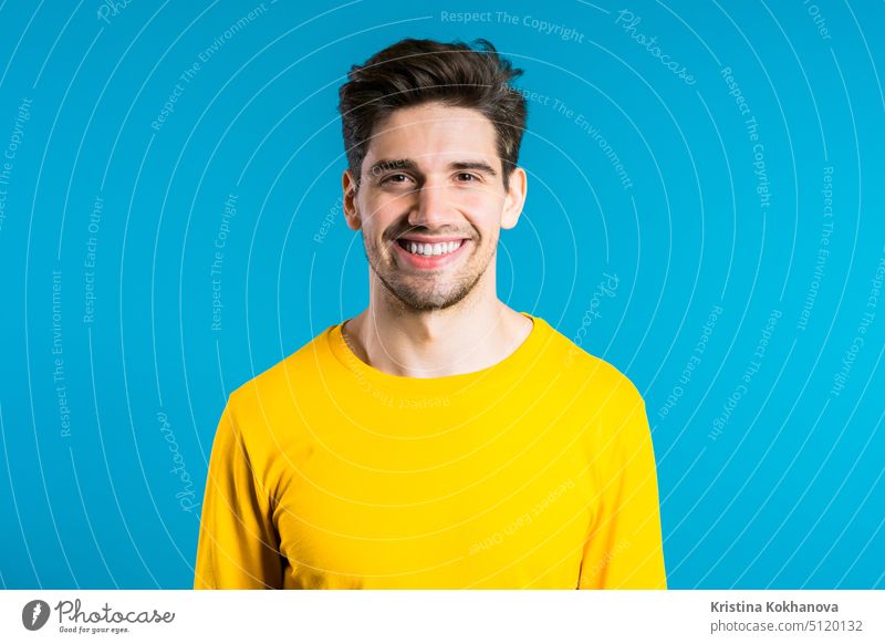 Handsome european man with trendy hairdo in yellow wear on blue studio background. Cheerful guy smiling and looking to camera. person portrait adult young