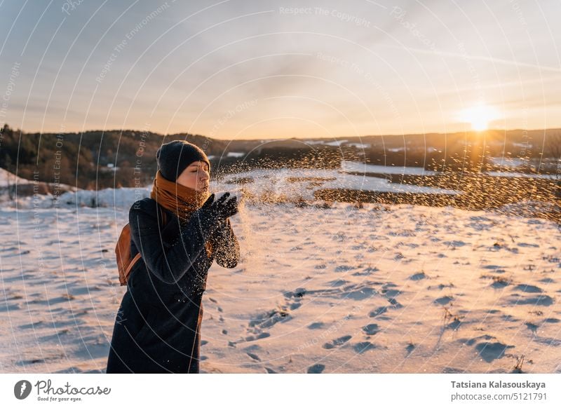 A woman blows in the palm of her hand with snow at sunset in winter warm clothes female people person European White adult mid adult hold one Single person