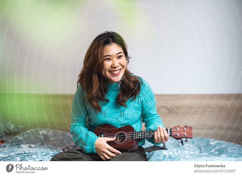 Young woman having fun playing Ukulele in her studio apartment real people candid girl young adult millennials Millennial Generation asian Japanese happy