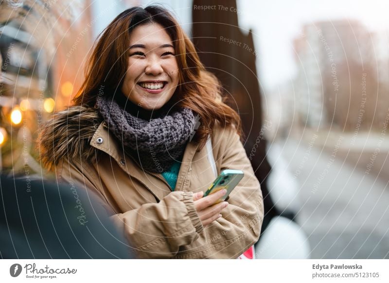 Young woman using mobile phone while standing at bus stop real people candid girl young adult fun millennials Millennial Generation asian Japanese happy smiling