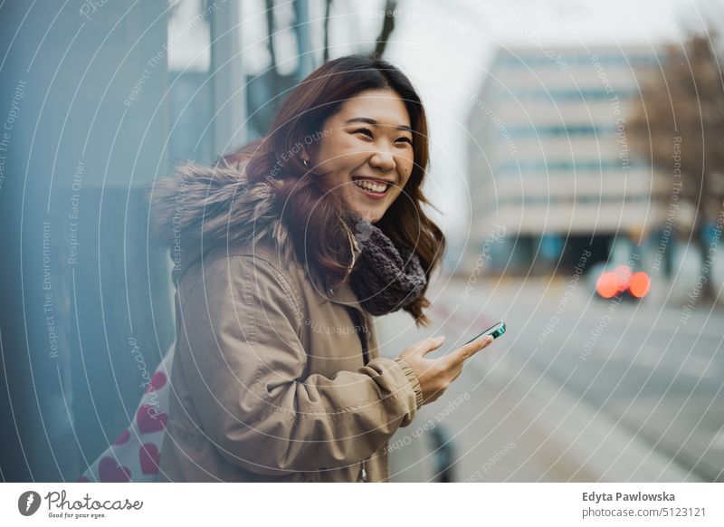 Young woman using mobile phone while standing at bus stop real people candid girl young adult fun millennials Millennial Generation asian Japanese happy smiling
