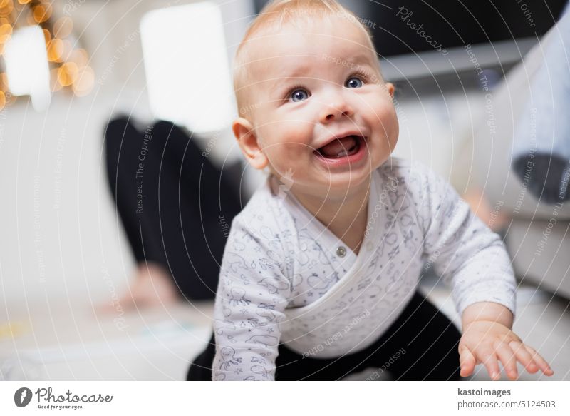 Cute infant baby boy playing, crawling and standing up by living room sofa at home. Baby playing at home newborn childhood development toy entertainment active