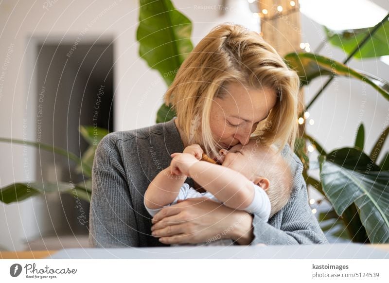 Portrait of young mother cuddling and kissing her adorable little child while sitting at the table at home. Sensory stimulation for baby development family