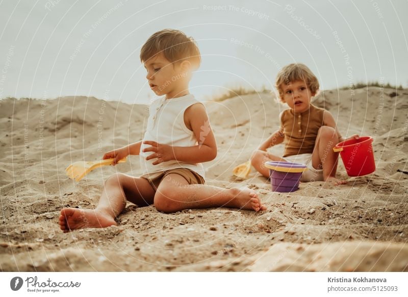 Twin brothers play on beach in sand with their plastic toys