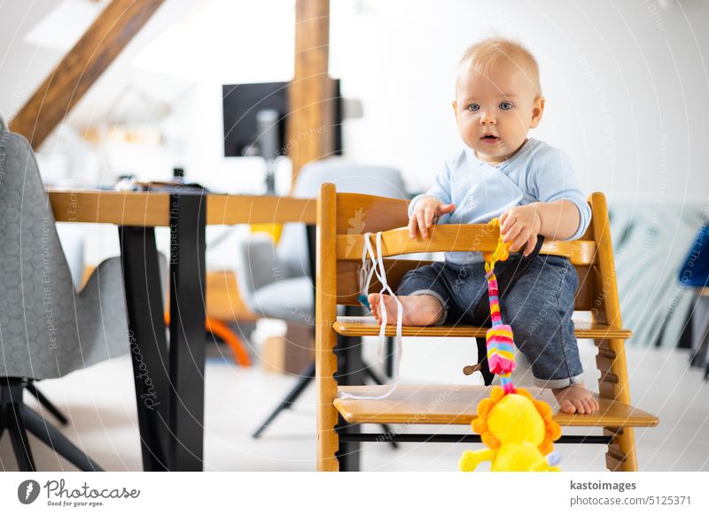 Happy infant sitting and playing with his toy in traditional scandinavian designer wooden high chair in modern bright atic home. Cute baby. child happy cute kid