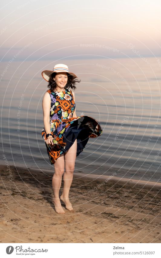 Happy young woman in flowery dress and summer hat dancing joyfully along seashore happy girl running beach sunset floral smiling female jumping sand water