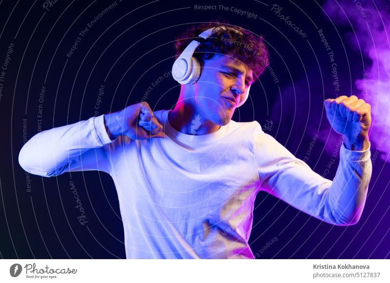 Positive man listening music with headphones, dancing on dark neon background. Stylish student guy enjoying life, active energy, inspired dance concept action