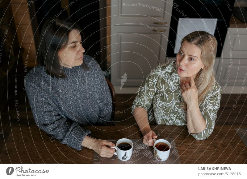 Two women talking at home. Girlfriends drinking cup of coffee in kitchen. friendship woman lifestyle female happy caucasian attractive beautiful adult smiling