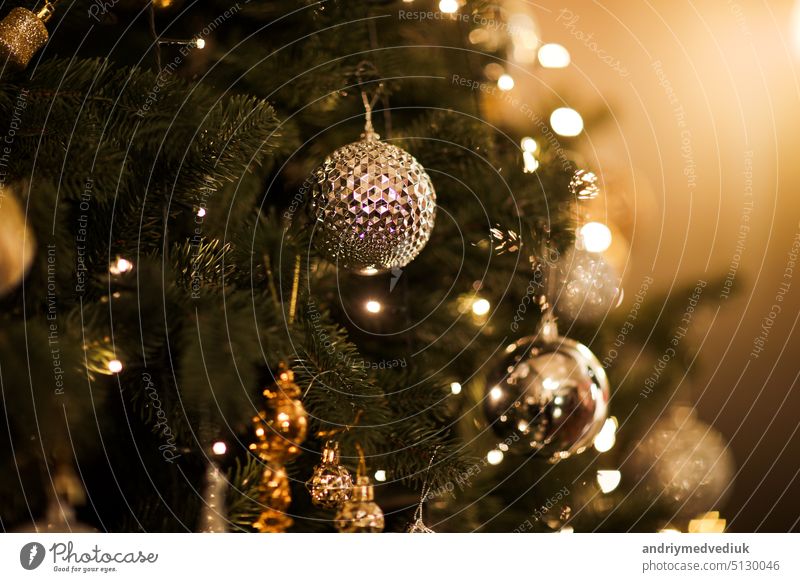 Close up view of beautiful fir branches with shiny golden bauble or ball, xmas ornaments and lights, Christmas holidays background. copy space. Decoration on christmas tree. Festive new 2023 year