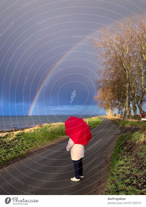 Lady with red umbrella marvels at double rainbow in Schleswig-Holstein Panorama (View) Copy Space left Copy Space right Copy Space middle Copy Space top