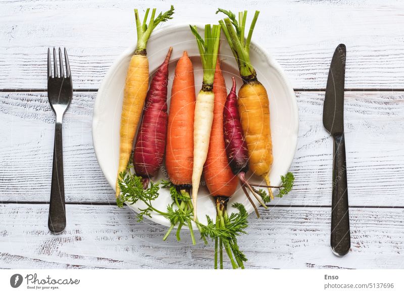 Rainbow carrots on plate, cutlery on wooden table, top view color various rainbow carrots multicolored purple white yellow orange fresh picked eating fork knife