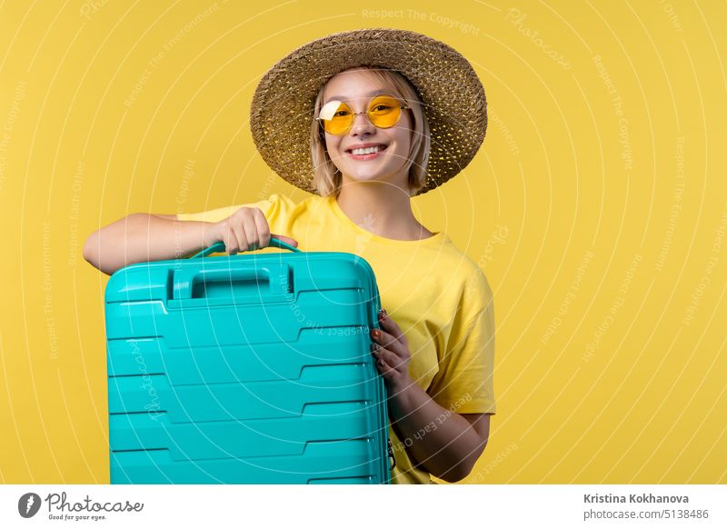 Young pretty woman with carry-on suitcase on yellow background. Teenager traveling with blue luggage bag for airplane hand baggage. Summer travel, vacation concept.