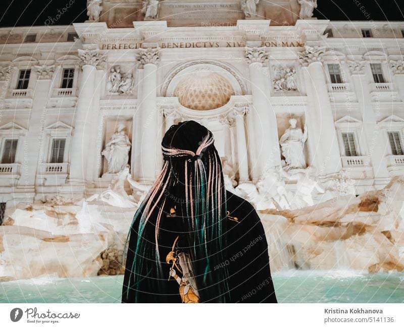 Girl with long braids standing near Trevi Fountain with illumination at night, most famous fountain in Rome, Italy. trevi art baroque italian italy monument