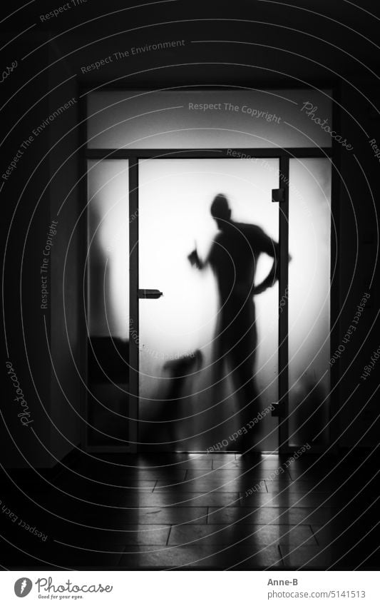 a man ( maybe a dog trainer ) asks a dog with raised index finger for attention behind the frosted glass pane of a door. dog training upbringing reprimand Dog