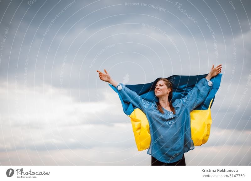 Smiling ukrainian woman with national flag on sky background. Portrait of young lady in blue embroidery vyshyvanka. Copy space. Ukraine, independence, freedom, patriot symbol, victory in war.