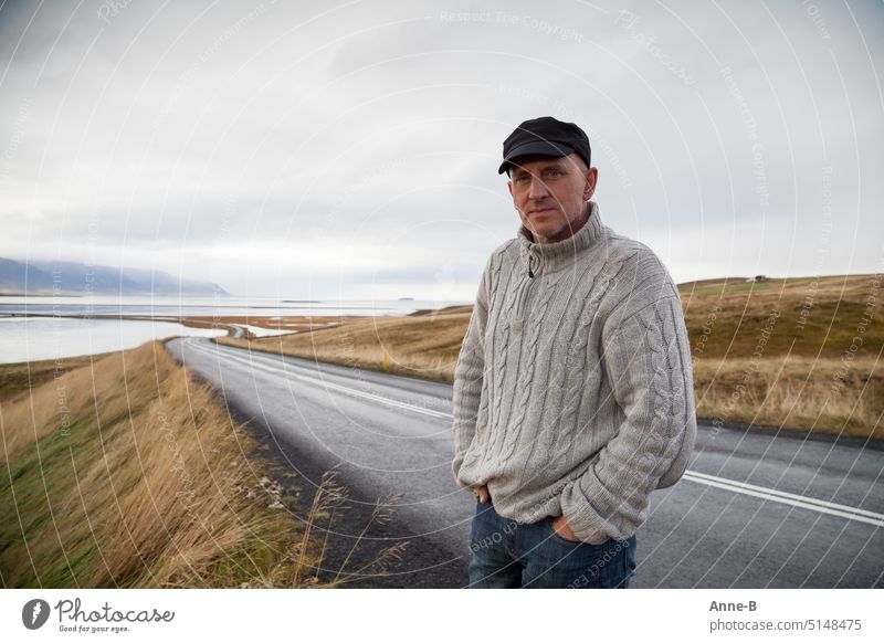 a man in a knitted sweater stands on a really lonely road in a beautiful hilly fjord landscape on a beautiful gray day Lonely Individual Man Street Fjord Hill