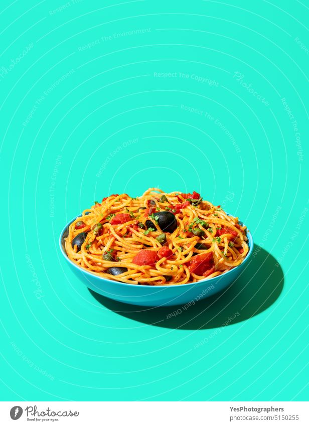 Spaghetti puttanesca bowl minimalist on a green background above blue bright capers carbs close-up color cooked copy space creative cuisine cut out delicious