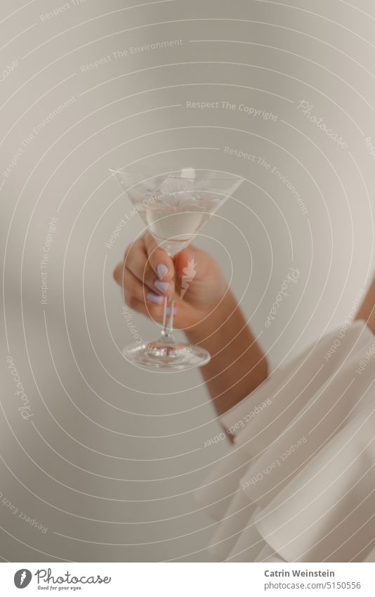 A female hand with purple painted fingernails holds a martini glass with petals. Hand Glass Martini cocktail Blossom leave White Wedding dress Cocktail Beverage
