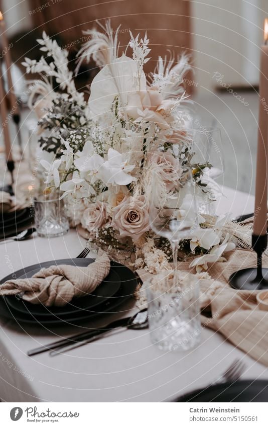 Table decoration in old pink and white. Centerpiece with roses, flowers and feathers. Also on the table are candles, black plates, glasses and cutlery. Bouquet
