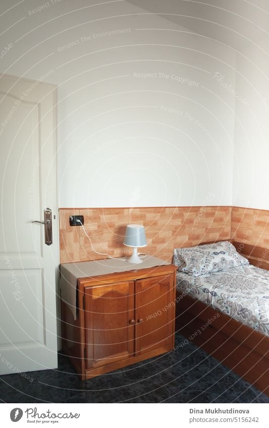 https://www.photocase.com/photos/5156242-very-simple-hotel-room-with-old-wooden-furniture-and-white-walls-interior-of-a-cheap-room-for-rent-in-a-house-renting-property-and-apartments-small-hotel-or-guest-house-interior-room-vertical-view-with-single-bed-and-bedside-table-with-lamp-dot-photocase-stock-photo-large.jpeg