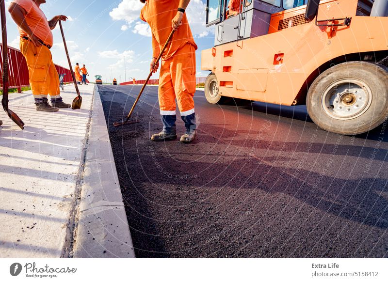 Worker with rake realign hot asphalt to correct measure Adjust Align Alignment Asphalt Asphalting Bitumen Blacktop Blacktopping Bridge Building Site