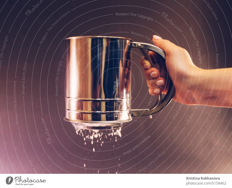 Female Hand sifting flour or sugar powder through sieve for baking. Close up baker bakery black blurred bowl bread burst cake caucasian chef closeup cloud color