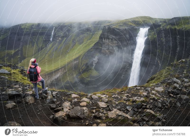 Woman with backpack and lilac jacket enjoying Haifoss waterfall of Iceland Highlands in Thjorsardalur Valley woman haifoss tourist travel nature mountain