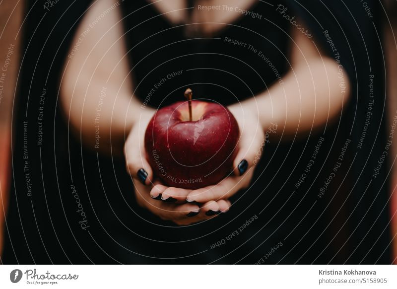 Woman as witch in black offers red apple as symbol of temptation, poison. anger art autumn background beautiful beauty bizarre celebration child contact costume