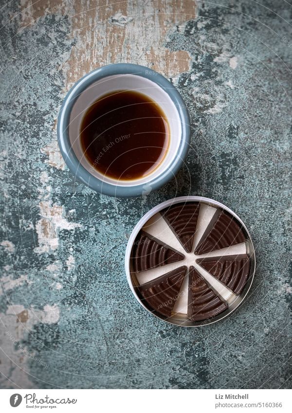 Top flay lay view of a cup of black coffee and a tin of chocolate triangles on a distressed board Coffee Coffee break To have a coffee Beverage Coffee cup