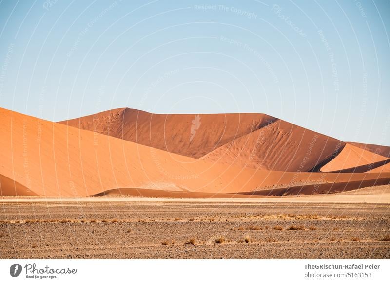 Sand dune with tracks against blue sky and sandstorm - a Royalty