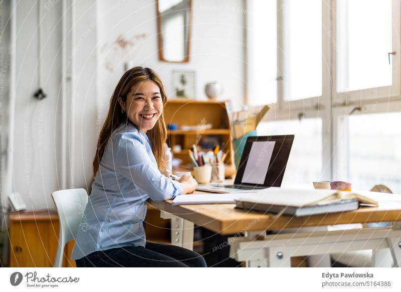 Young woman sitting at desk working on laptop real people millennials student indoors loft window natural girl adult one attractive successful confident person