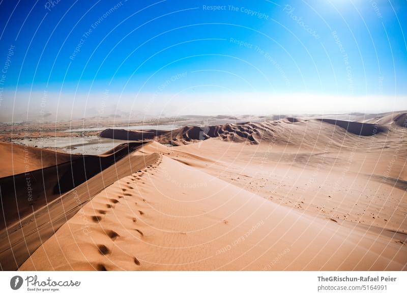 Sand dune with tracks against blue sky and sandstorm - a Royalty