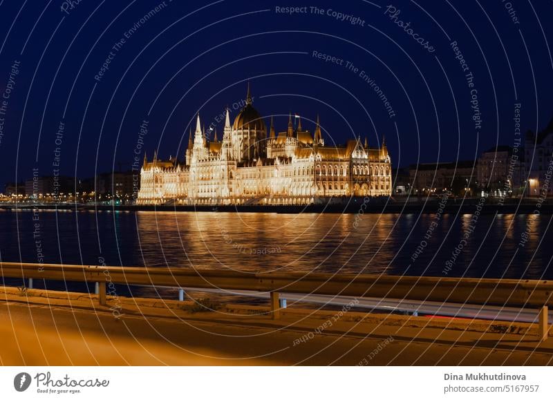 Hungarian Parliament Building in Budapest reflected in the water of Danube at night, photographed on sunny day with blue sky. Domed Neo-Gothic style architecture. Famous landmark for sightseeing in Hungary postcard view.
