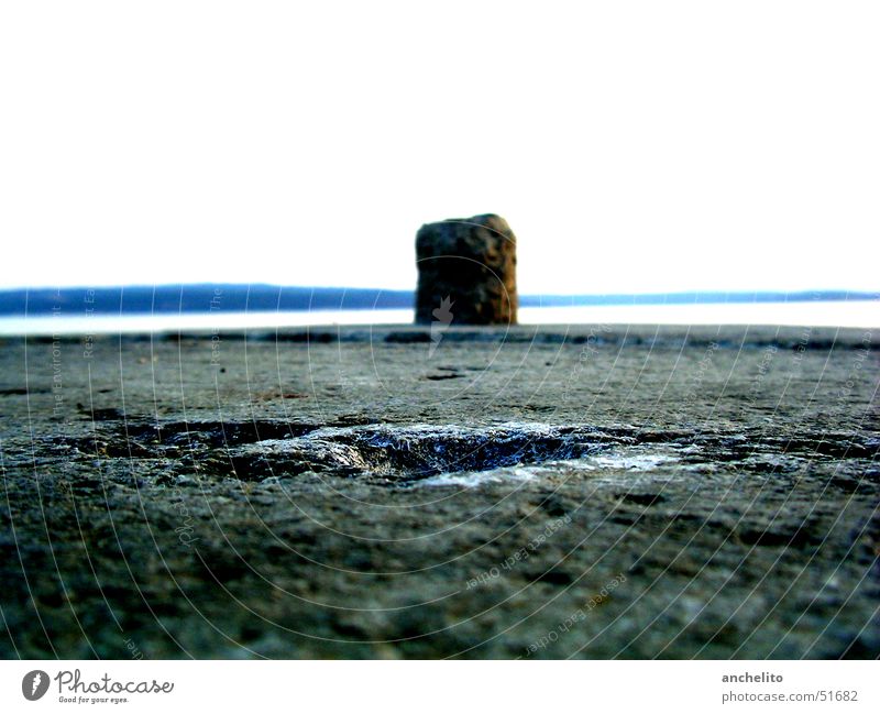 lonely bollard in front of the wide sea Bollard Asphalt Ocean Lake Gray Sky White Loneliness Far-off places Fastening Beach Coast pollard Stone Floor covering