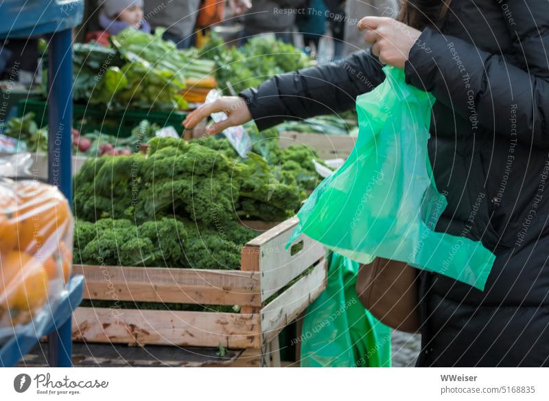 At a weekly market, a woman buys fresh vegetables and puts them in a green plastic bag Green Vegetable Markets Farmer's market Vegetable stand Shopping Box up