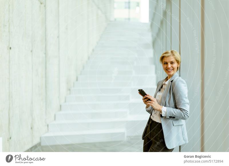 Businesswoman using mobile phone on modern office hallway adult attractive beauty brunette business business person businesspeople businessperson businesswoman