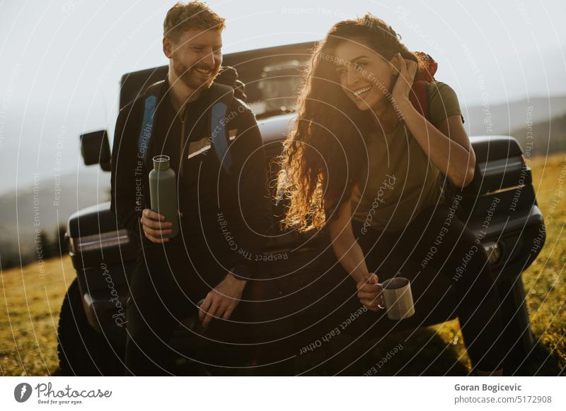 Young couple relaxing on a terrain vehicle hood at countryside adult adventure attractive auto automobile man break calm car caucasian day drink drinking enjoy